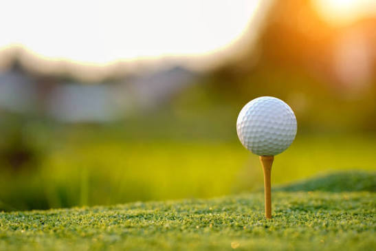 A premium golf ball resting on a tee in freshly mowed grass at golden hour